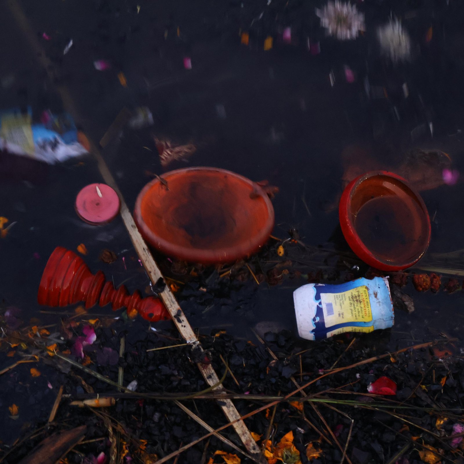 Ritual remains and offerings floating in dark water at the ghat
